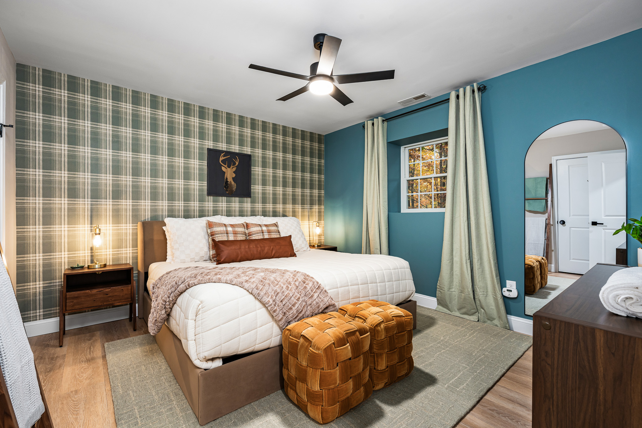 This bedroom pairs modern comfort with classic lodge charm, featuring a king bed against a plaid accent wall, earthy green tones, and warm textures. A cozy retreat with style and personality.