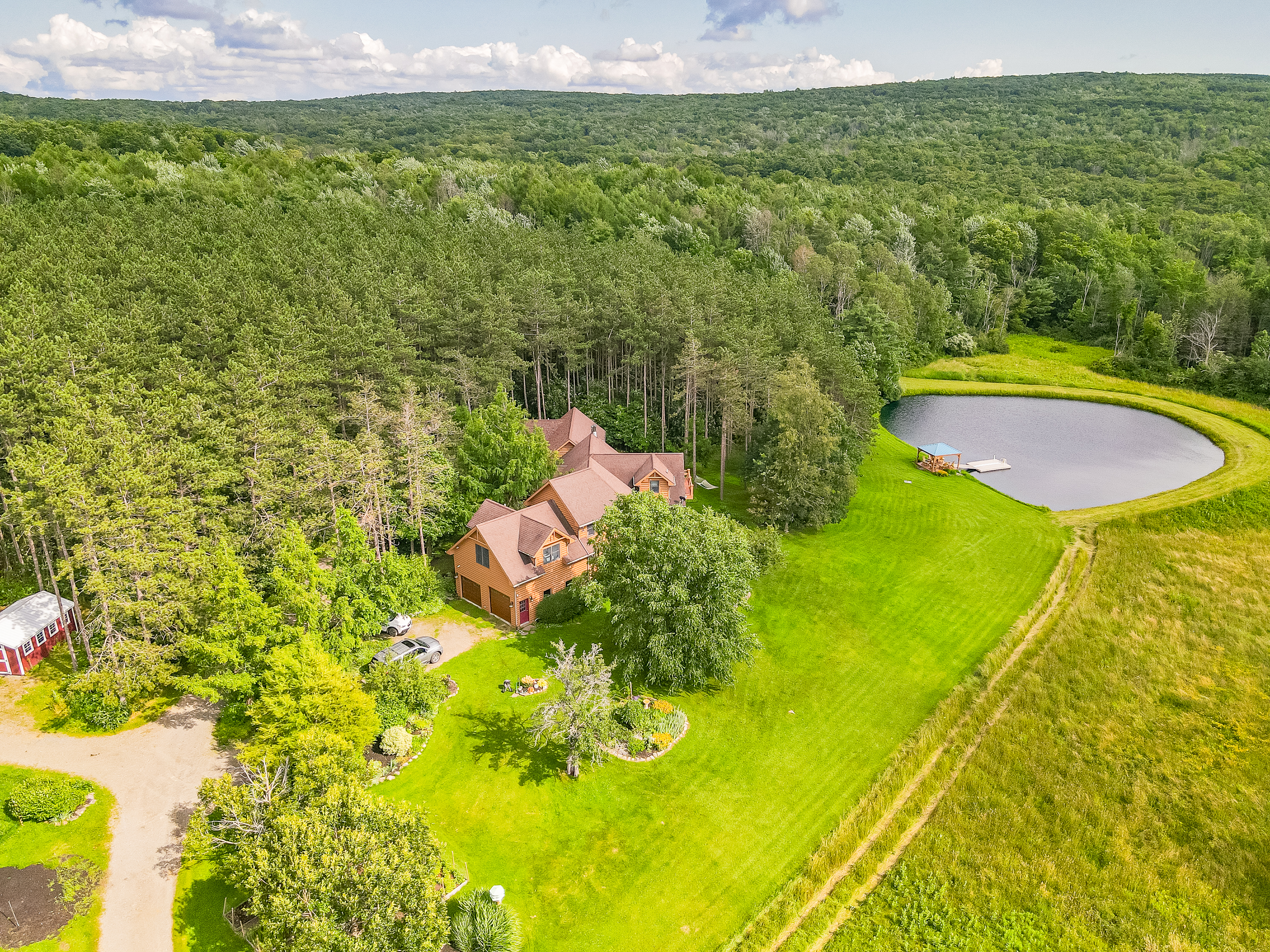 Stunning bird’s-eye view of the home nestled in trees, complete with a sparkling pond and open green fields.