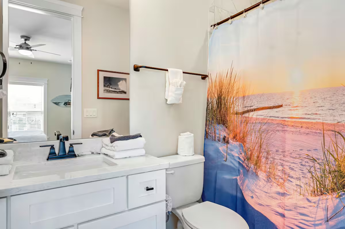 Attached private bath with coastal flair, featuring a sleek vanity, beach-inspired decor, and a shower/tub combo for a refreshing retreat.