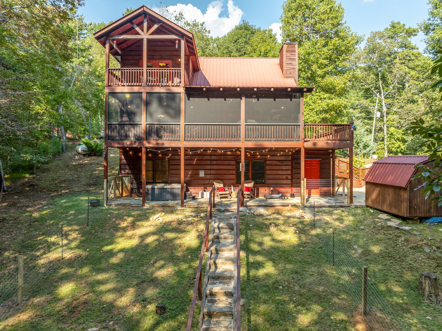 From above, the drone captures a peaceful haven — a private porch off the king bedroom and a screened-in porch with a gentle bench swing and BBQ. Down back, the hot tub bubbles beside an elevated dog bed, complete with water bowl for your furry travel bud!