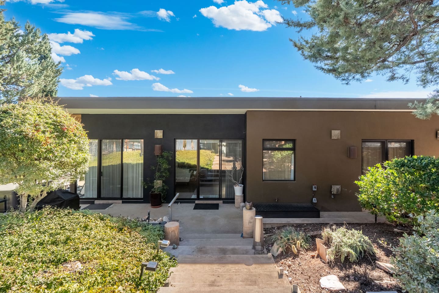 Clean modern exterior with a welcoming entry, surrounded by manicured landscaping and mature trees.