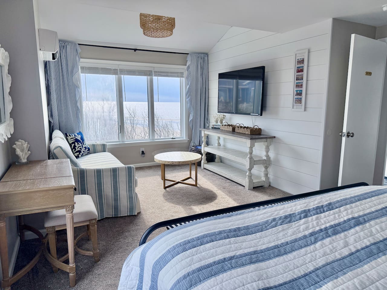 Enjoy a serene coastal retreat featuring a comfortable sitting area with a striped sofa, a scenic window view, and a wall-mounted television, all designed to provide a perfect, relaxing environment for your vacation.