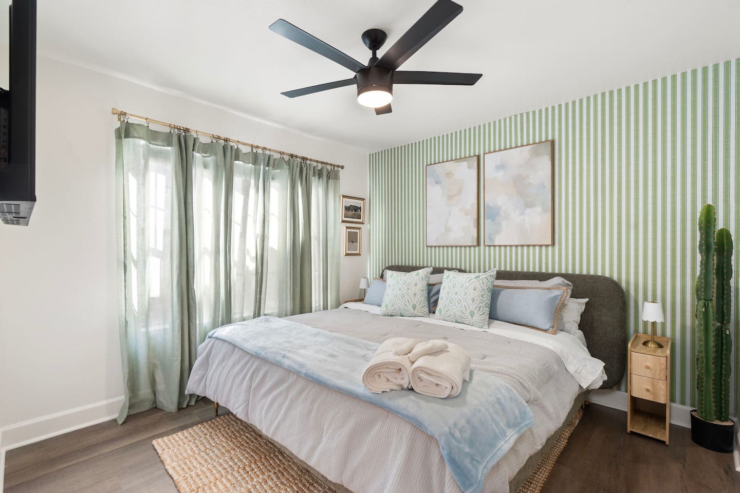 Bright guest bedroom with green striped accent wall, soft linens, and natural light—a calming retreat with thoughtful style.