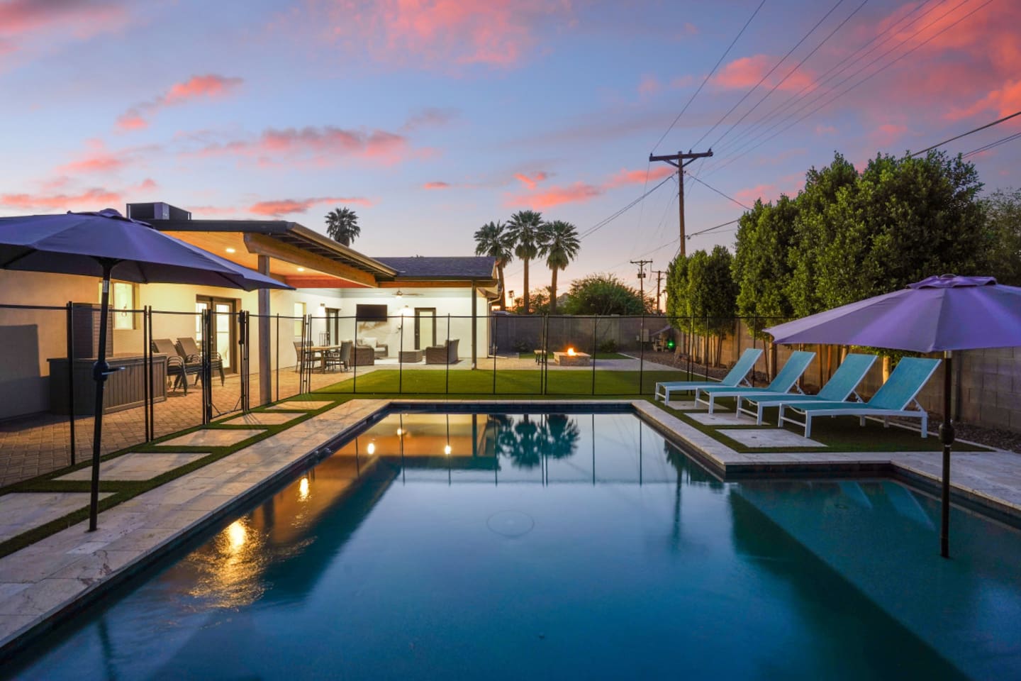 Private backyard pool at sunset with lounge chairs, umbrella shade, fire pit seating, and a bright outdoor space 