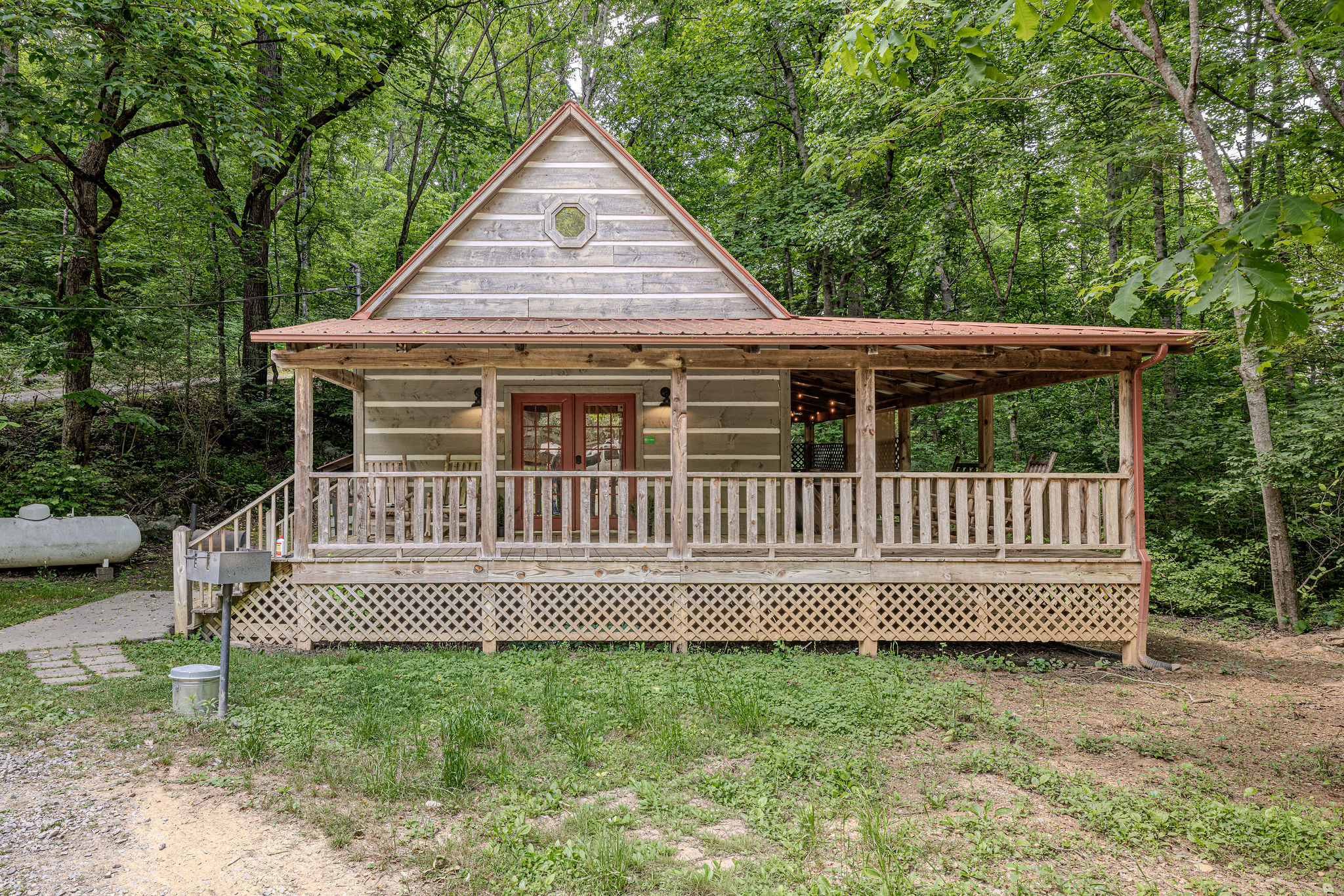 Wide covered porch and tall trees on all sides.
