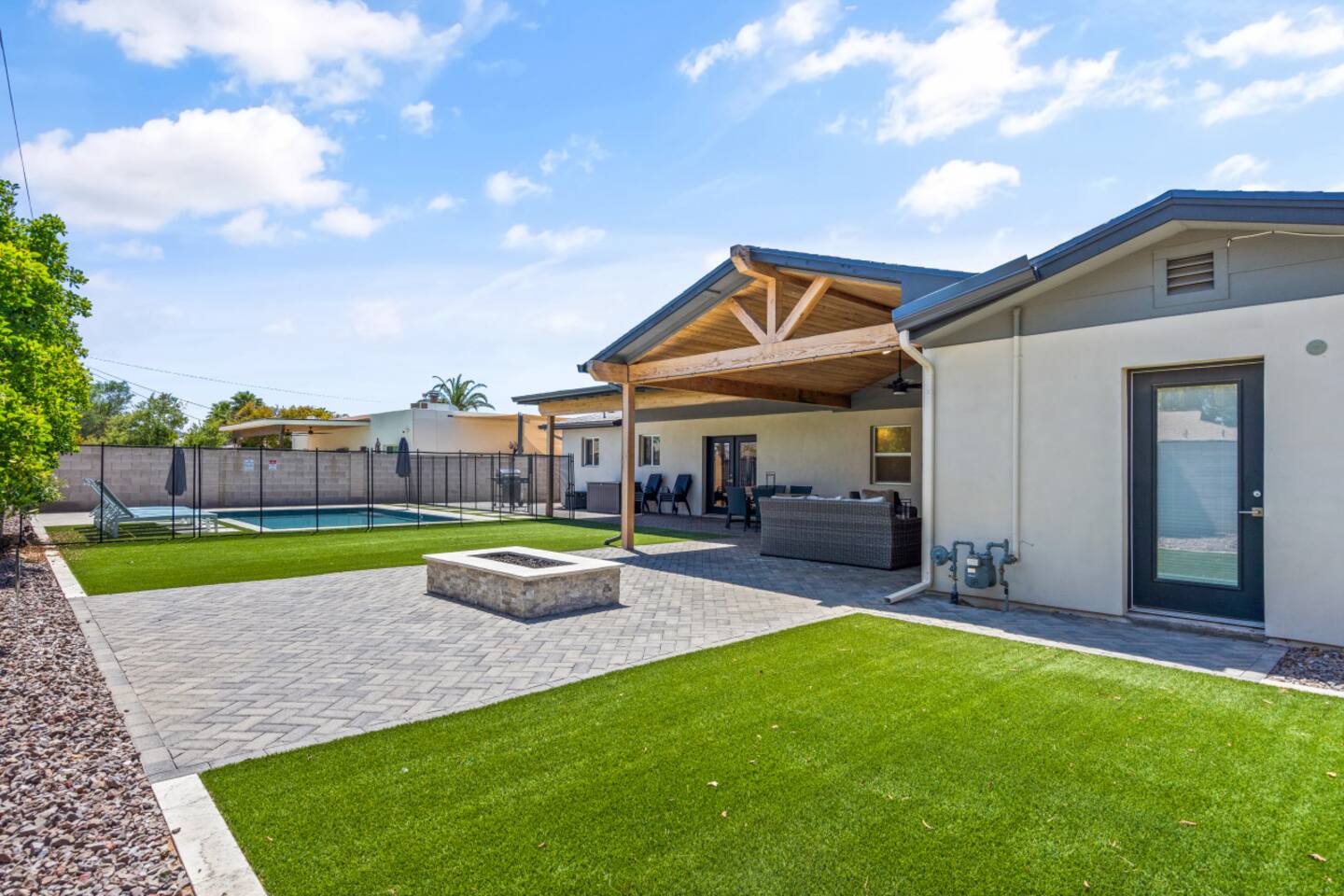 Outdoor living area with shaded lounge space, fire pit, and a clear view toward the pool.