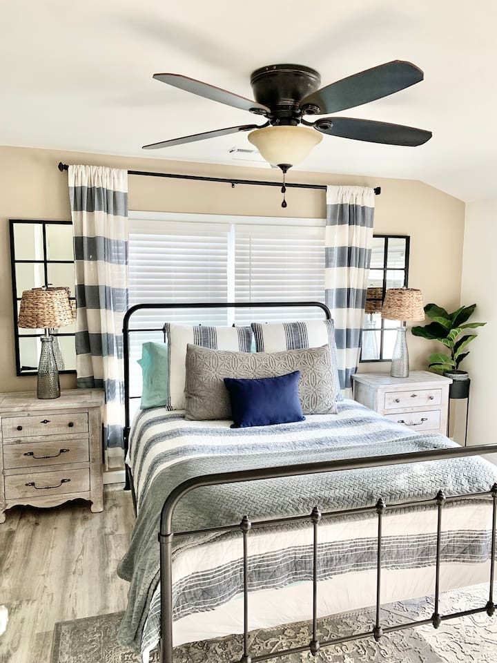 Rest easy in this coastal-inspired retreat. Featuring a classic wrought iron bed frame, plush nautical bedding, and rustic wood nightstands, this bright and airy room provides a peaceful sanctuary for a perfect night's sleep.