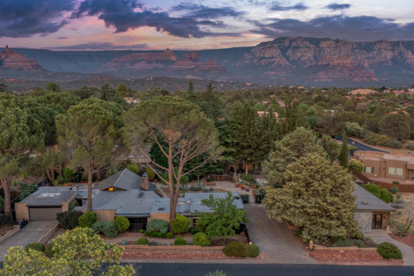 Stunning aerial at sunset — surrounded by lush greenery with sweeping Sedona red rock and mountain views in every direction.