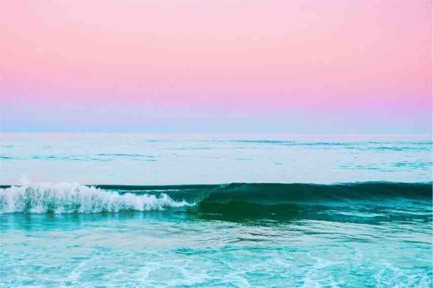 Tranquil ocean waves under soft pink and blue skies evoke calm and serene beach vibes.
