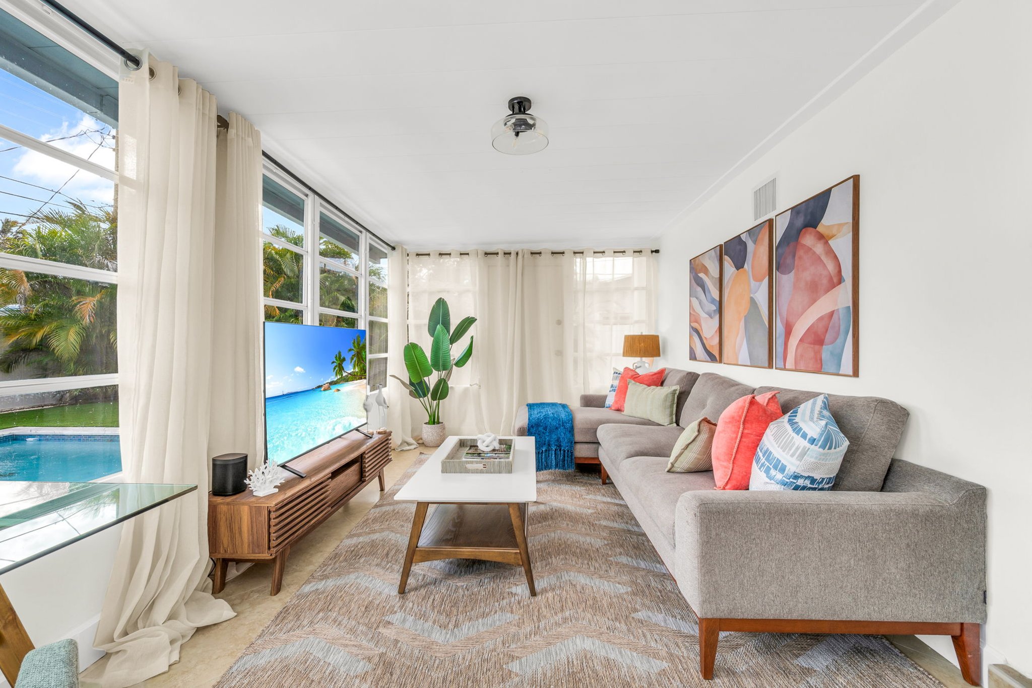 A beautifully designed Florida sunroom with wrap-around windows, modern furnishings, a Smart Fire streaming TV, and tranquil pool views—ideal for lounging, morning coffee, or working in style.