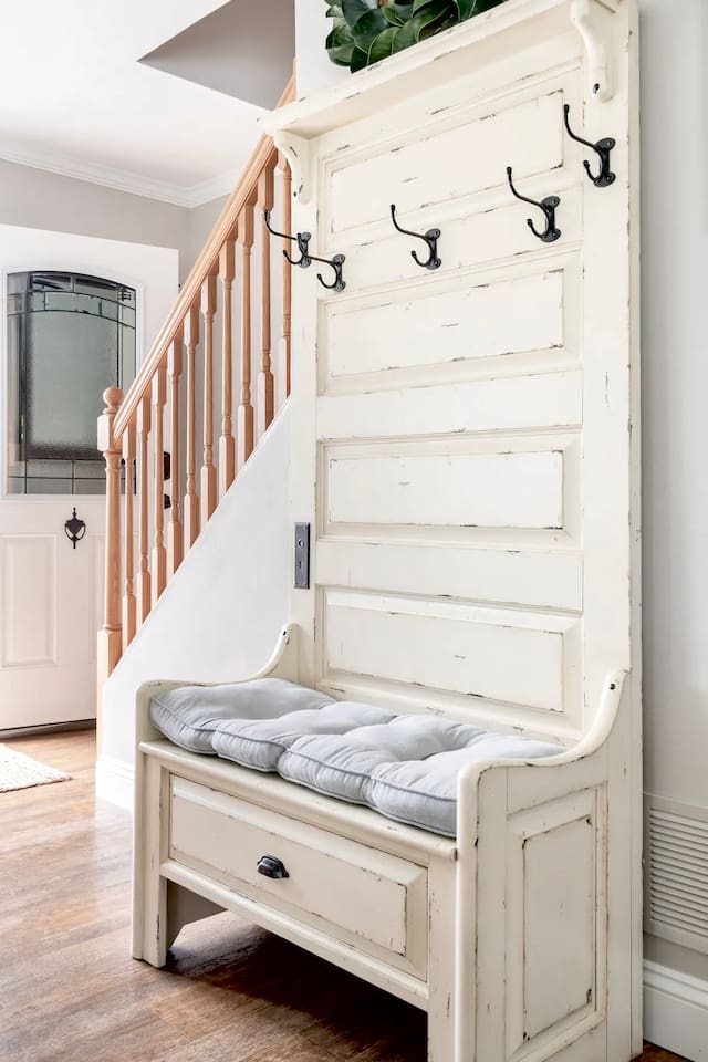 This charming, vintage-style hall tree bench provides a comfortable spot to sit and change shoes. Its distressed white finish and soft cushion add a touch of farmhouse style to the entryway.