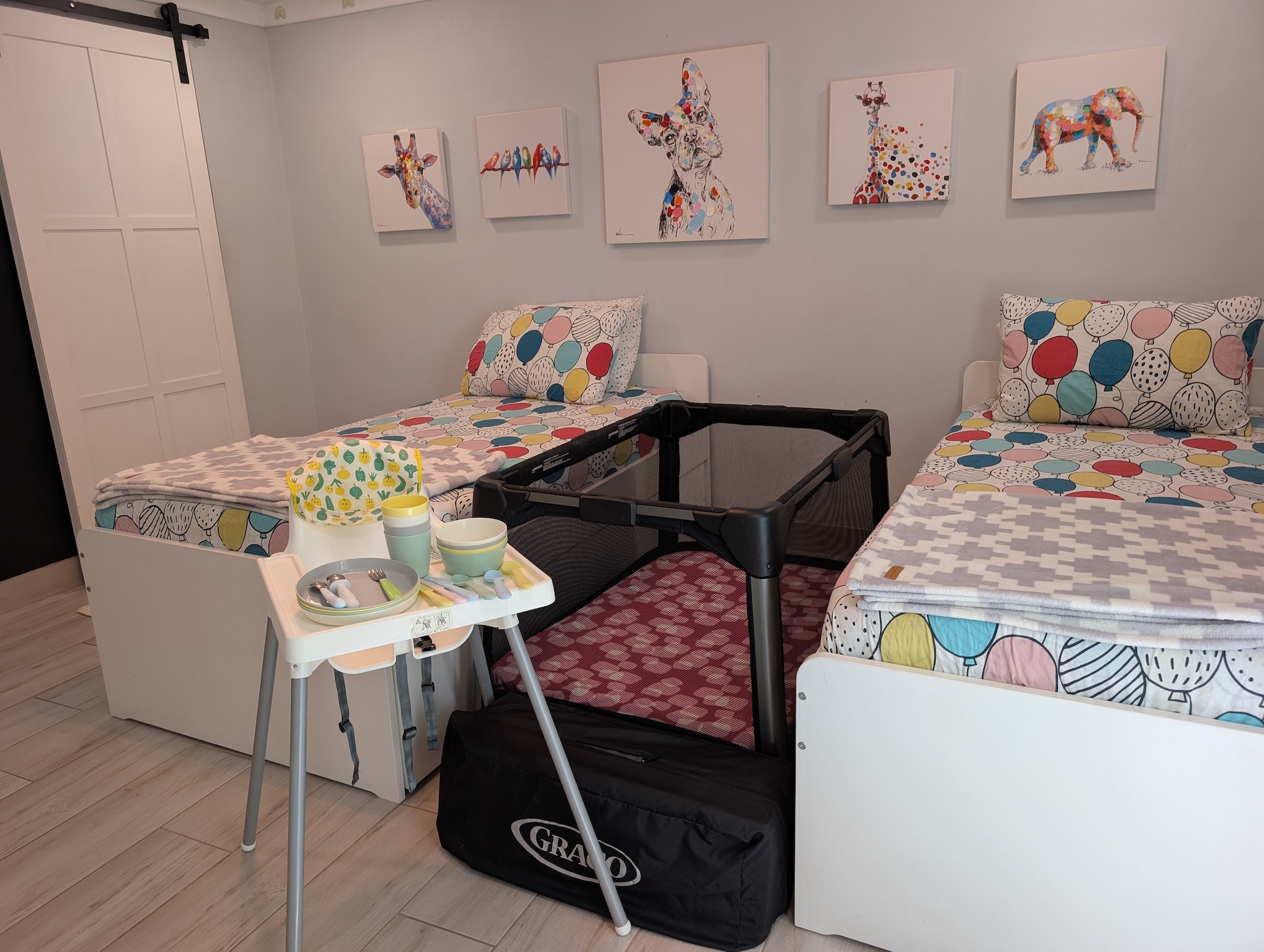 Kids' bedroom at Villa Coral featuring twin beds, colorful animal wall art, a set up Graco Pack 'n Play crib, a high chair, and toddler dinnerware in Dorado, Puerto Rico.