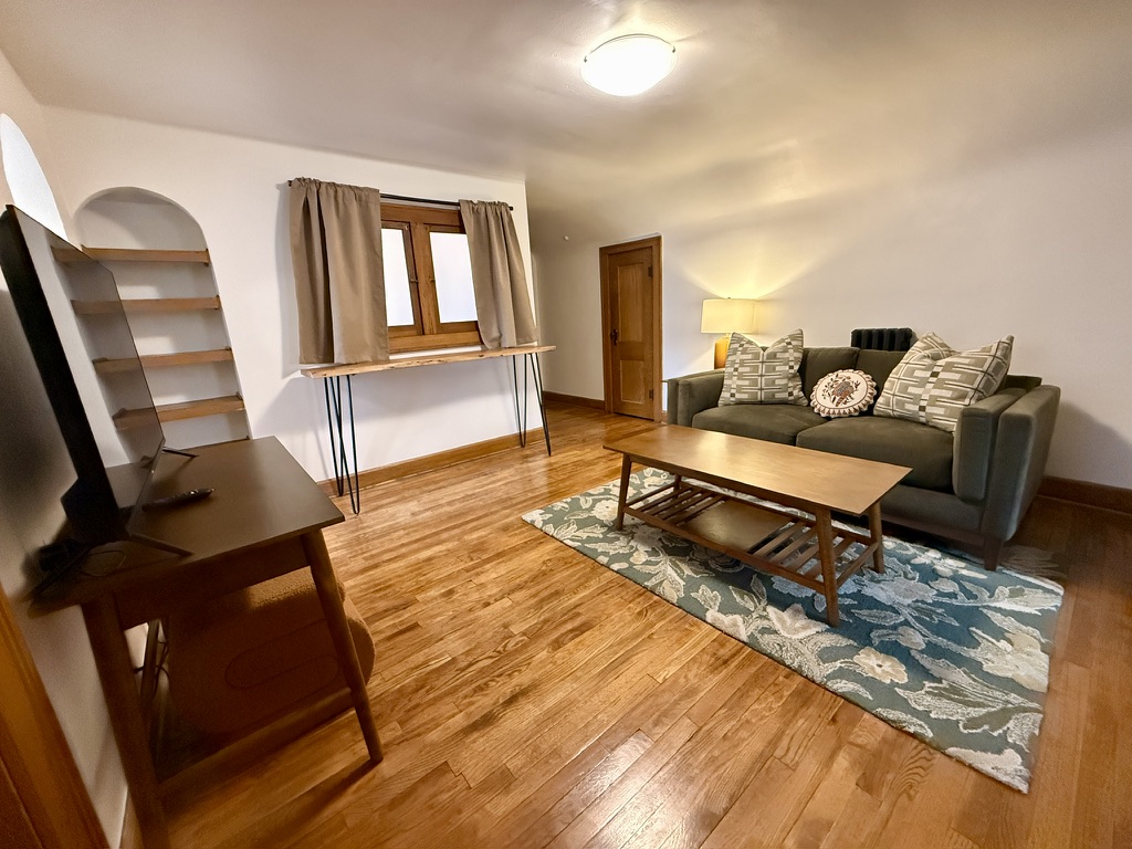 Living room with high-top table seating (stools not in photo), desk for dedicated work space, and built in shelves.