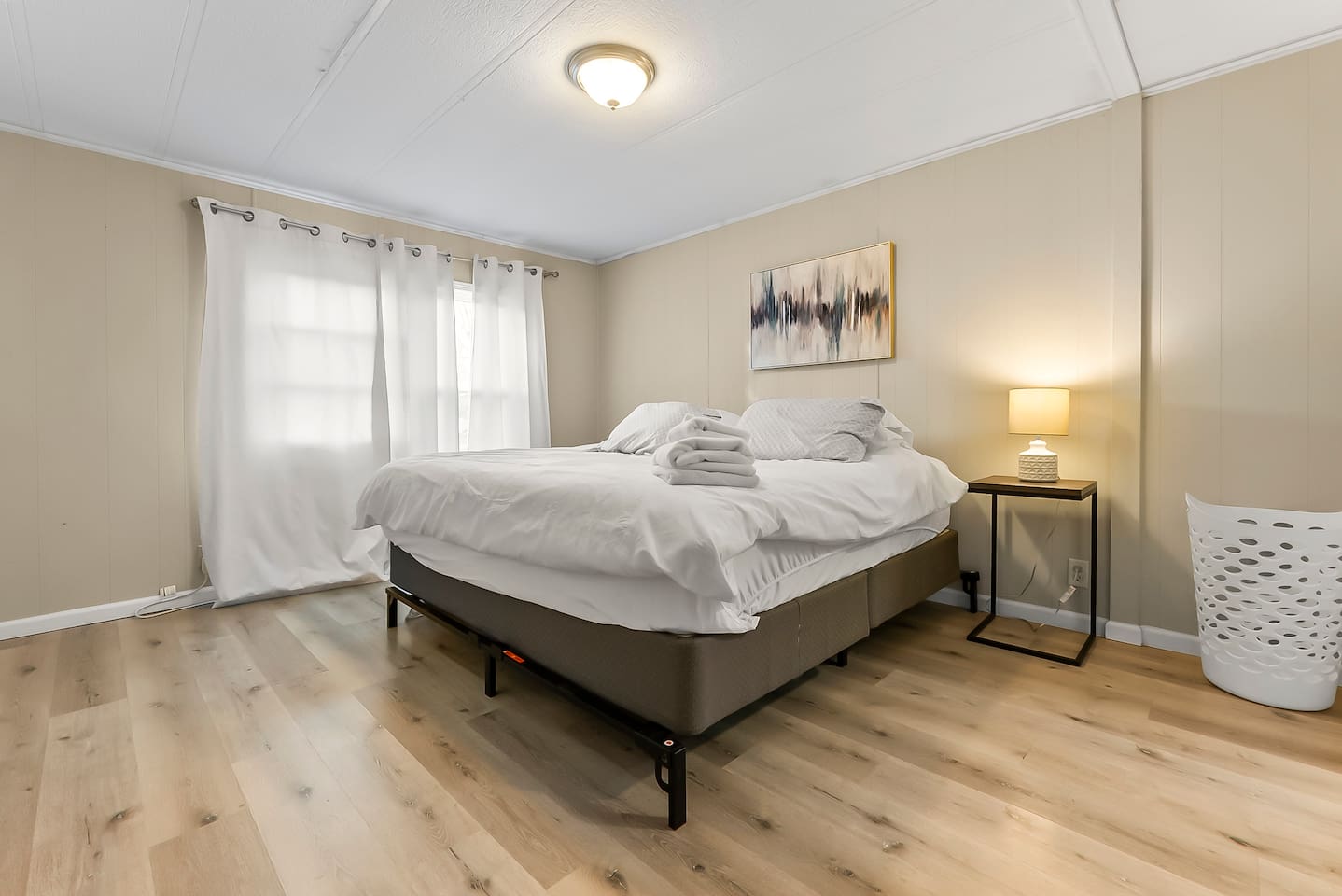 Spacious bedroom with a king-size bed, soft lighting, and natural sunlight from large windows.