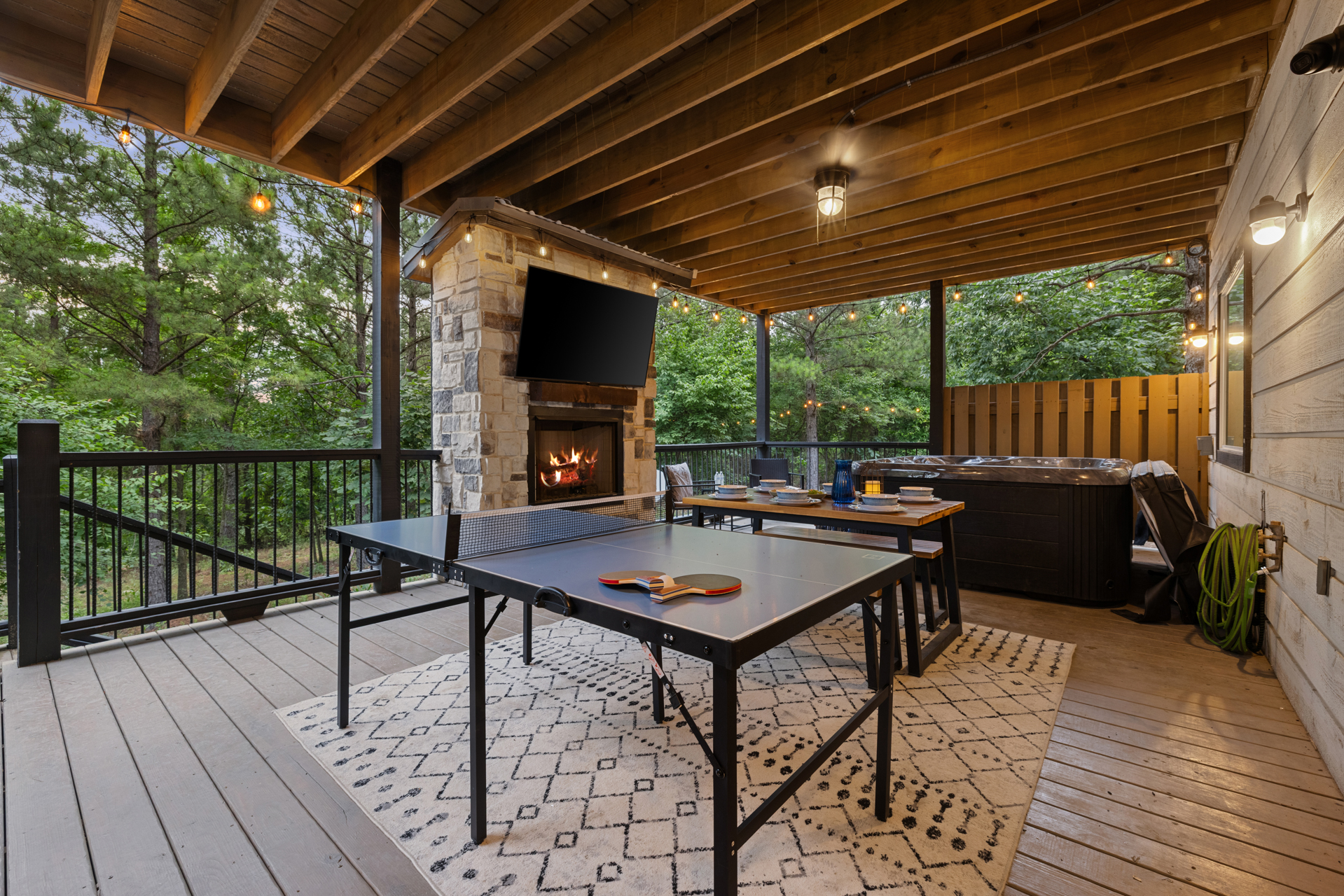 This inviting covered deck is designed for year-round outdoor enjoyment. Guests can relax in the private hot tub, gather around the cozy stone fireplace with an outdoor TV, enjoy meals at the dining table, or challenge each other to a game of ping pong. 