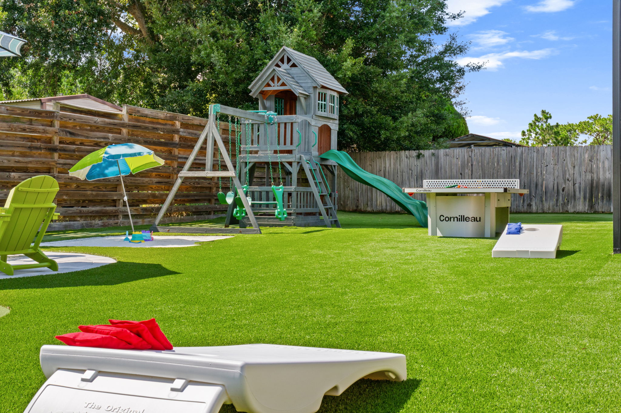 Non-stop backyard entertainment! This angle showcases our cornhole game boards ready for action, with the premium wooden playset, sand bunker area, and Cornilleau ping-pong table spread across the beautiful artificial turf.