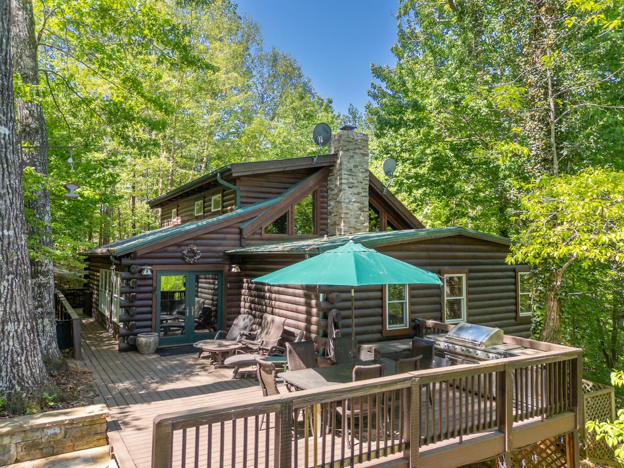 Spacious main-level deck surrounded by peaceful wooded views, outdoor seating, dining space, and a grill perfect for relaxing, entertaining, and enjoying fresh mountain air.