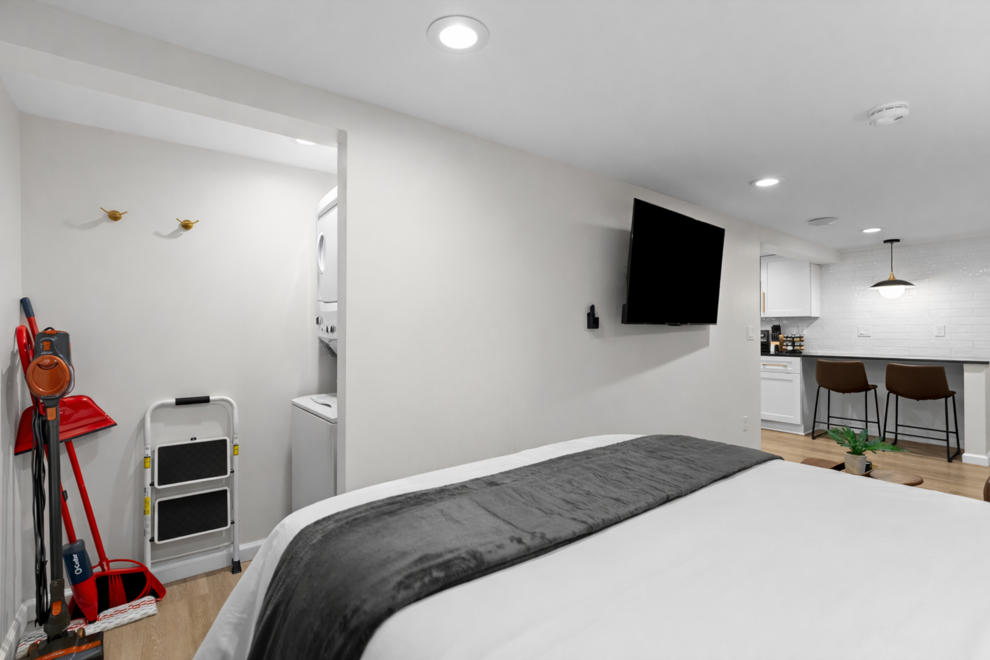 Comfortable sleeping area with a plush bed, wall-mounted smart TV, and an open layout that flows easily into the kitchen and living space.