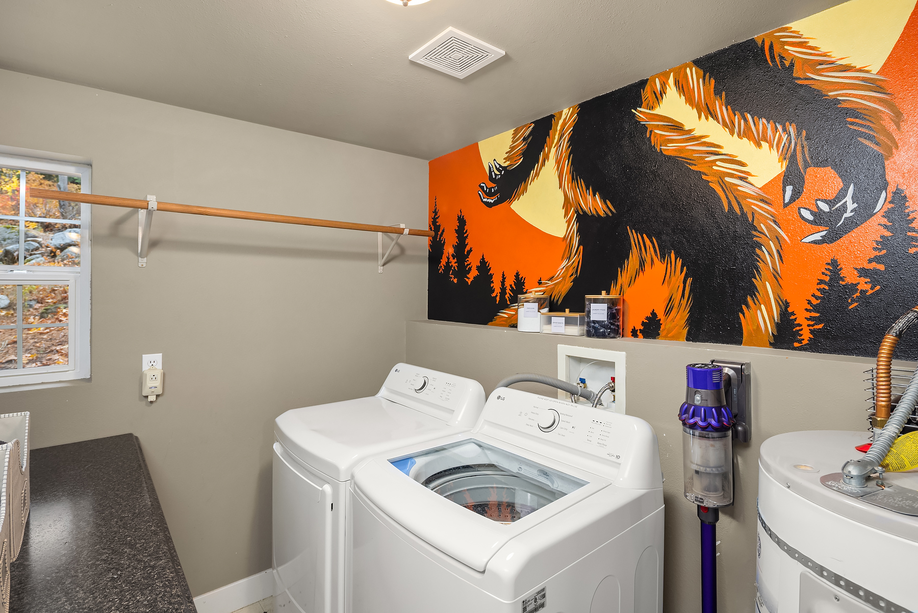 Lower level laundry room with washer and dryer, detergent pods and fabric softeners provided with fun mural