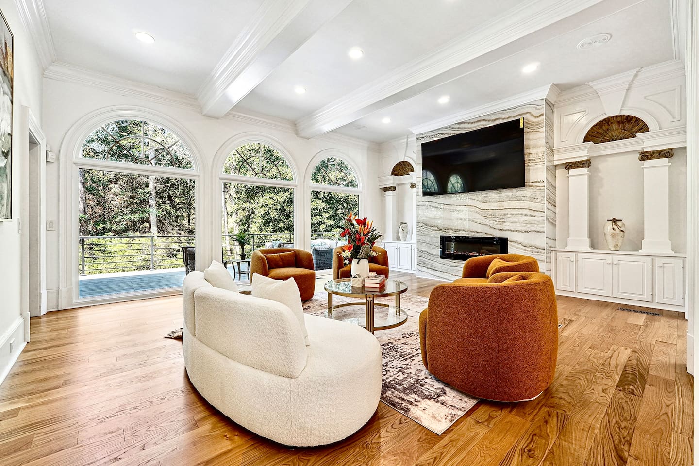 Located straight ahead from the front entry, this main-floor living room showcases a striking modern design with a round shaped contemporary sofa, four orange accent chairs, a smart TV, and a fireplace for a warm, elevated lounge experience.