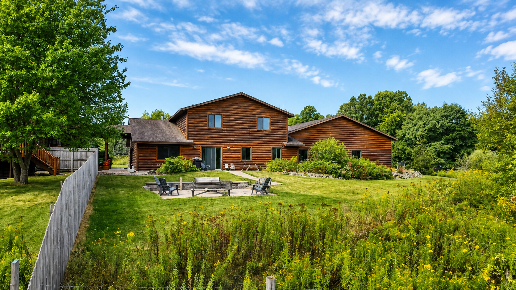 Wide exterior view of the lodge, patio, fire pit, and surrounding grounds, showcasing the outdoor gathering space and peaceful Northwoods setting your group can enjoy throughout the stay.