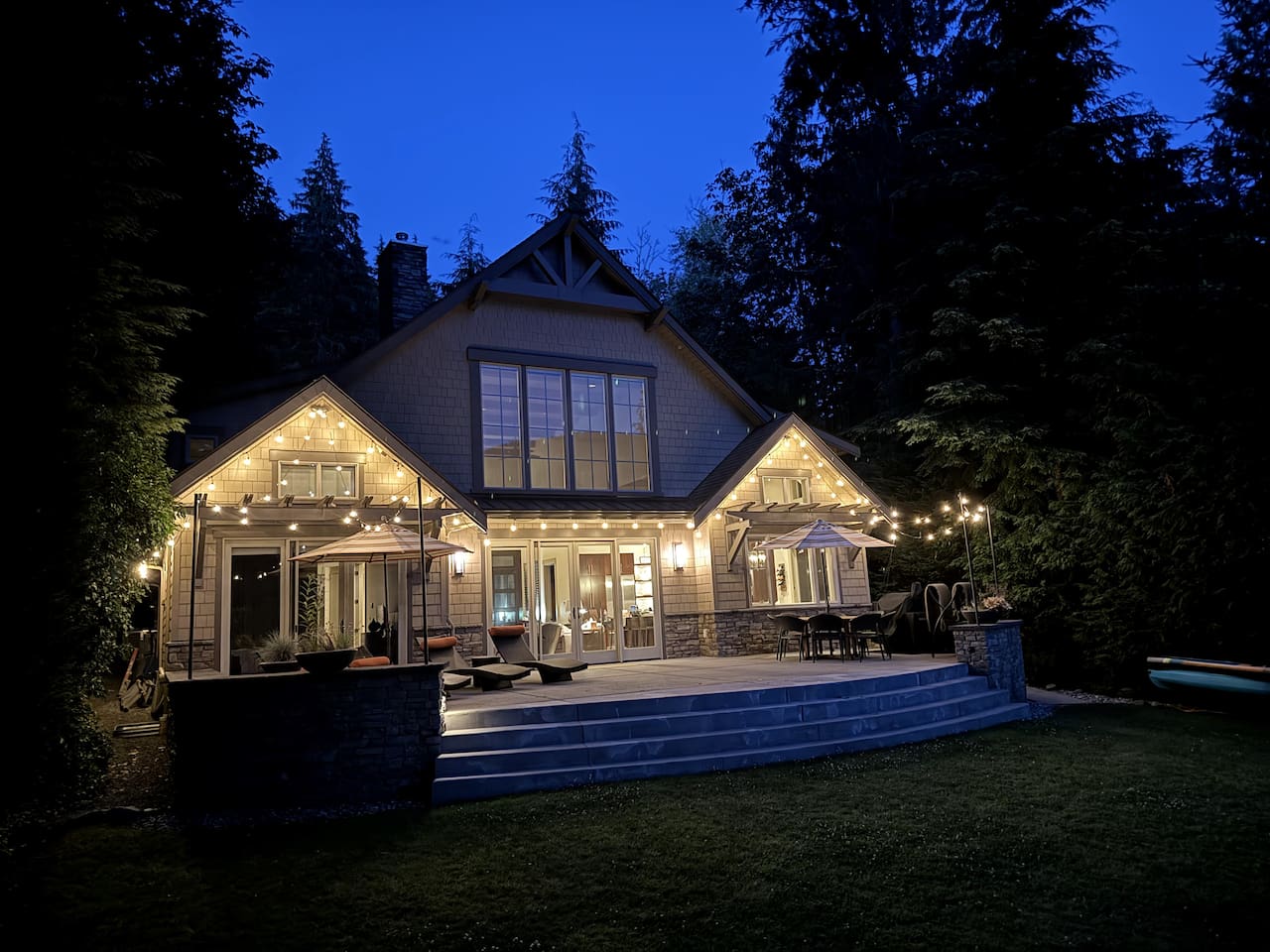 Twilight view of the house exterior, warmly lit by patio lights.