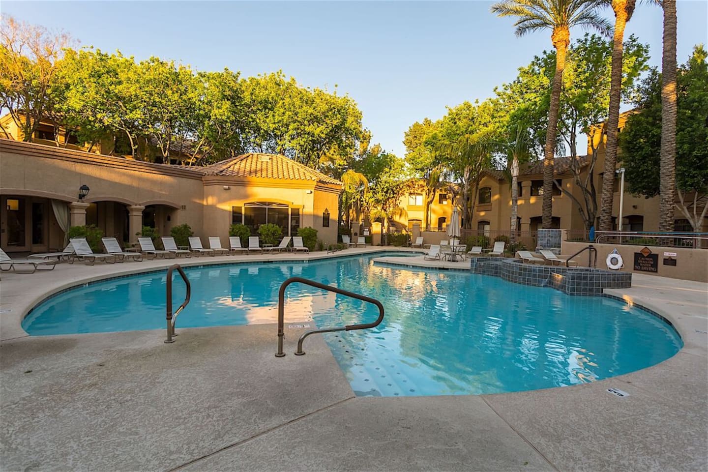 Community pool area with lounge chairs, shaded seating, and a resort-style outdoor setting.