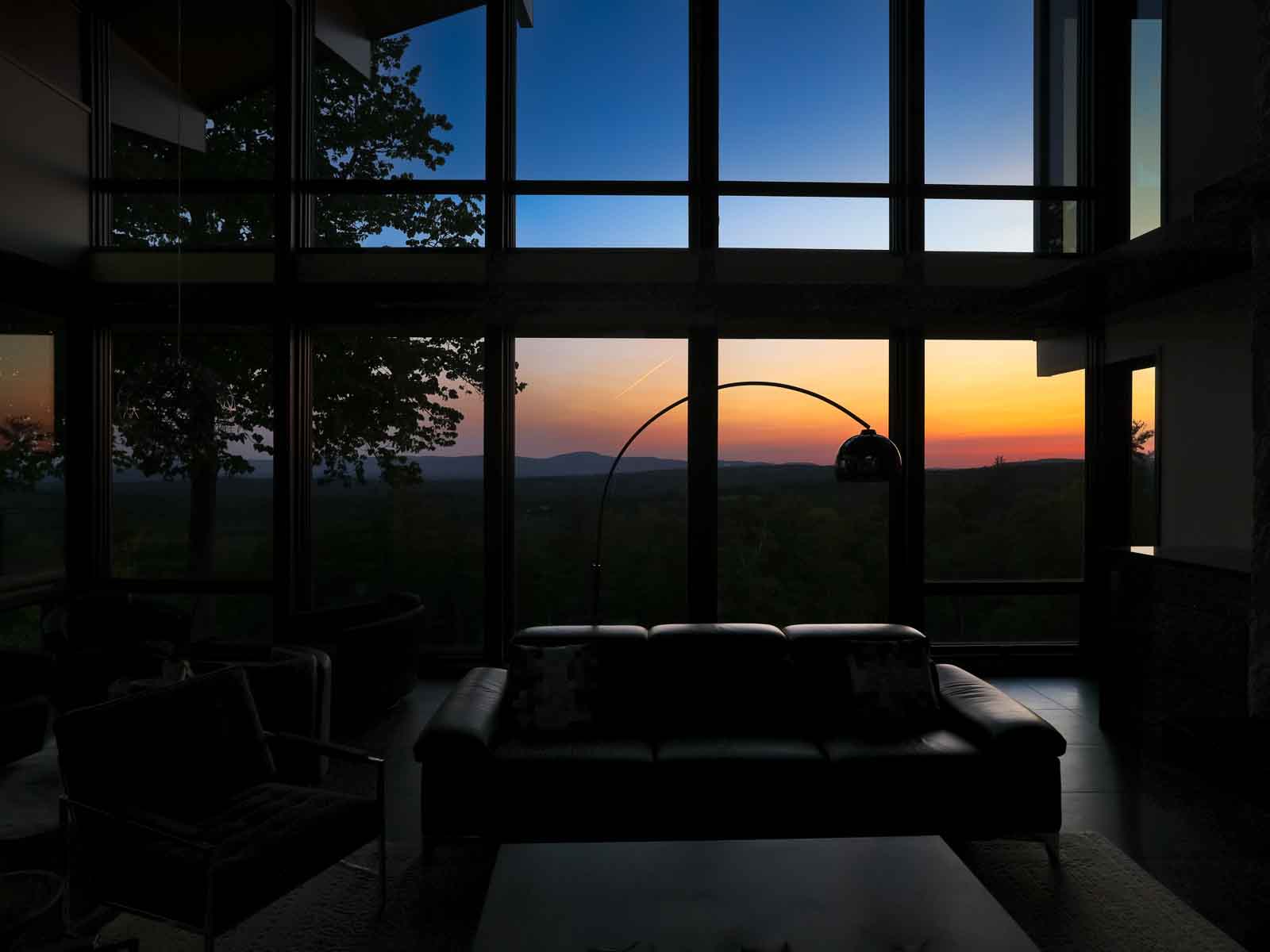 Great room at dusk with amber sunset through floor-to-ceiling windows &mdash; Sunset Falls Berkshires