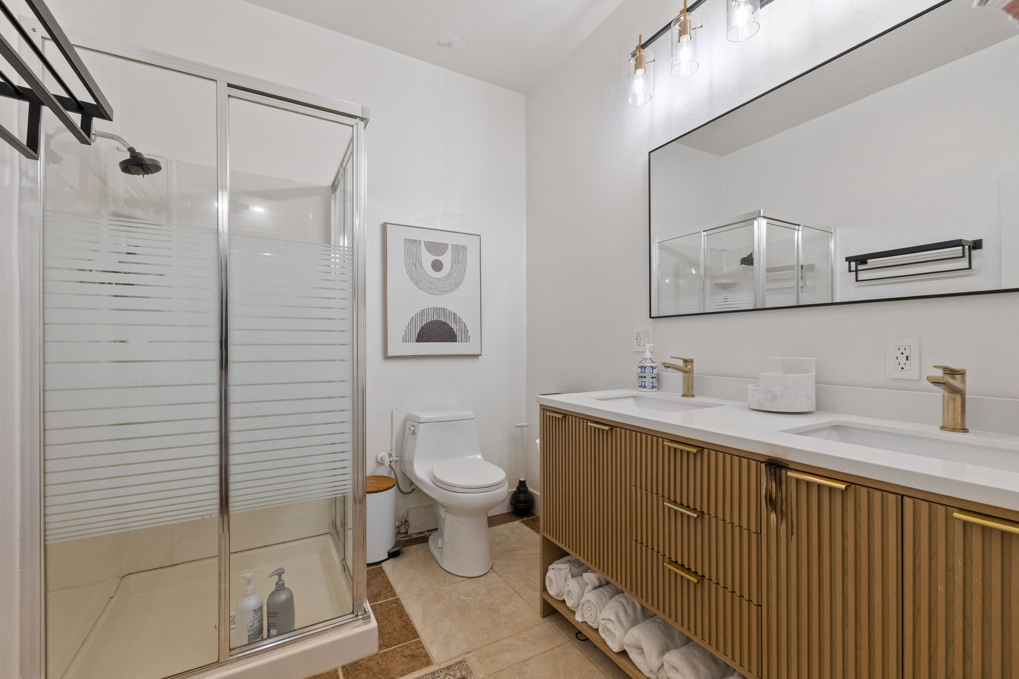 Downstairs bathroom with dual sinks, shower, toilet, storage for many towels and towel rack.