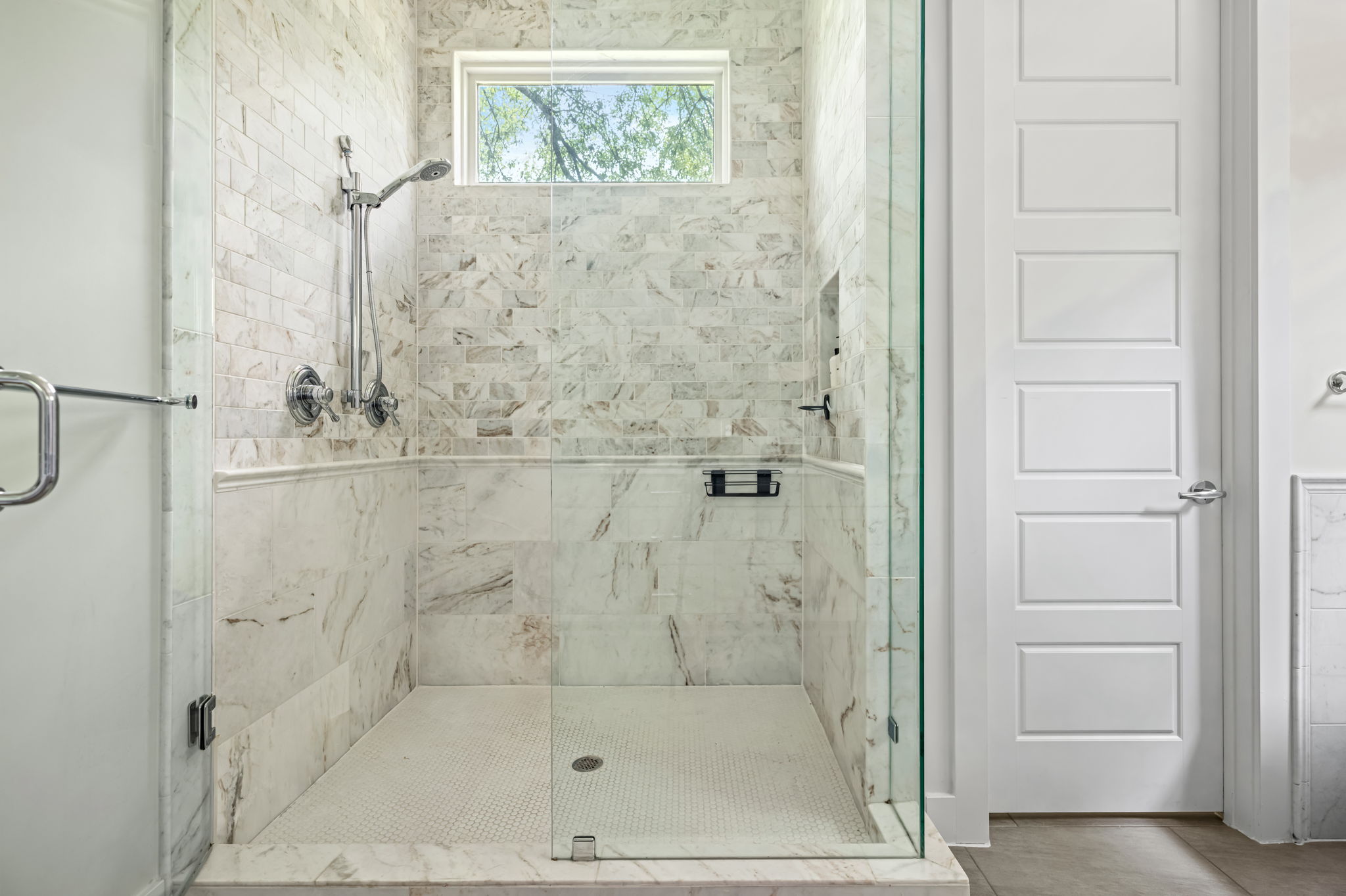 Frameless glass walk-in shower with marble tile surround and natural light — sleek, modern.
