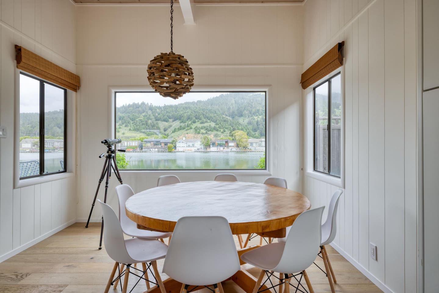 - Bright dining area with round wooden table and seating for eight guests  
- Stylish windows offer panoramic water and hillside views while dining  
- Unique pendant light adds charm to this airy, scenic gathering space  
