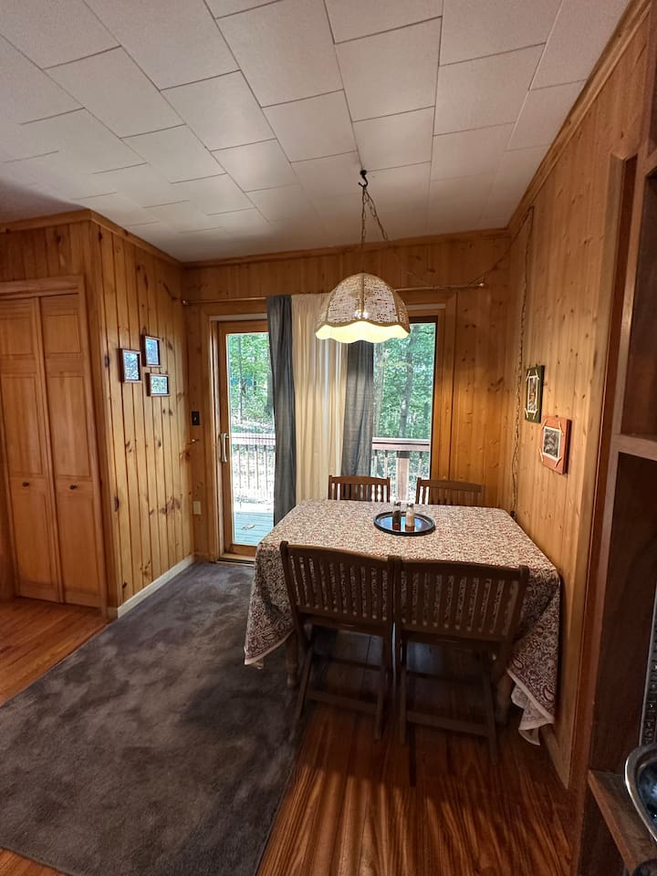 The dining area features a leaf table with four chairs, plus two extras stored in the cabin. It sits in front of a sliding glass door, offering a nice view and natural light. Great for meals, puzzles, or planning your day.  