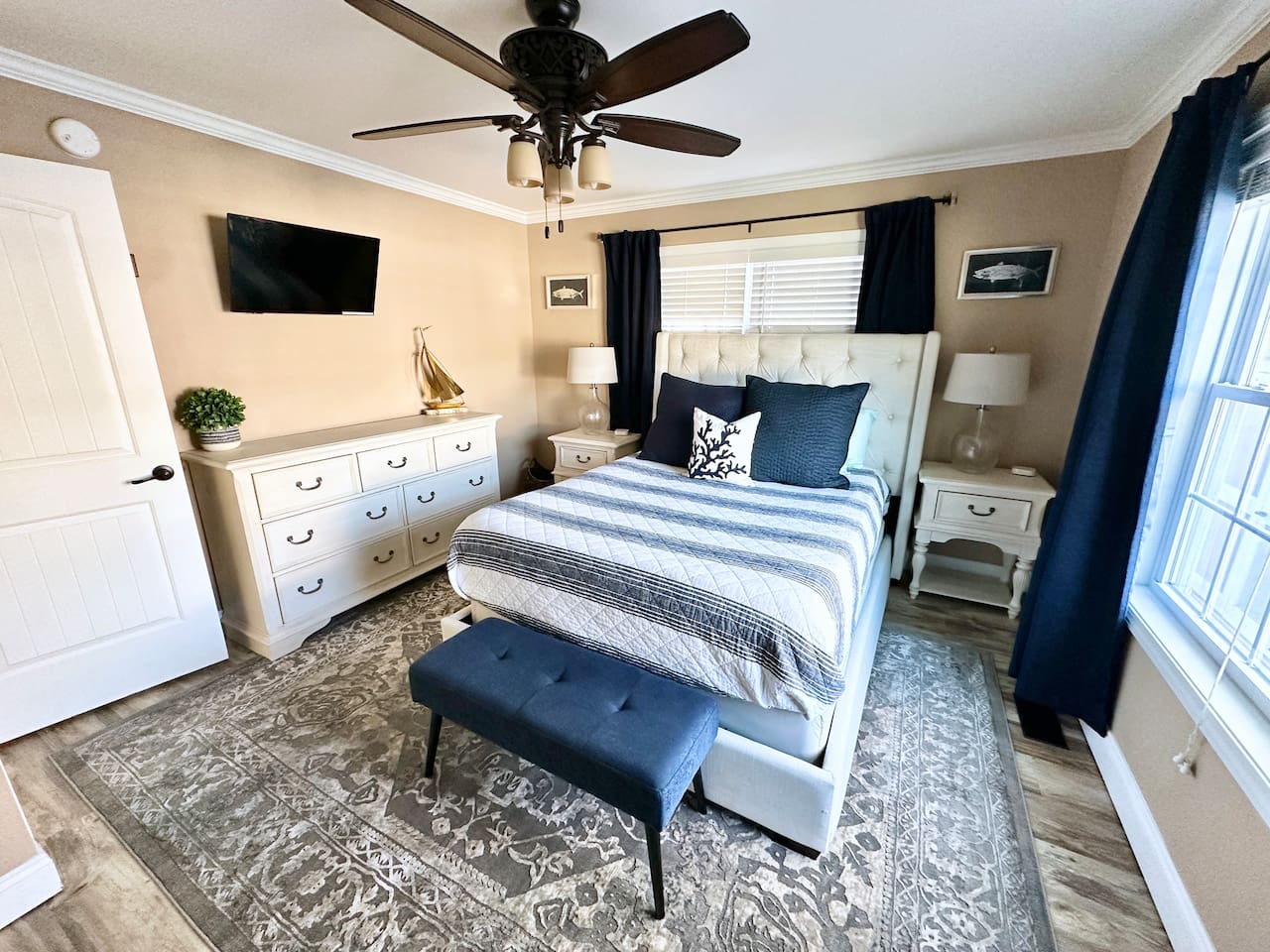 This nautical-inspired bedroom offers a tufted queen bed, a mounted TV, and a spacious dresser. A blue upholstered bench, patterned area rug, and coastal accents create a relaxing retreat for your stay.