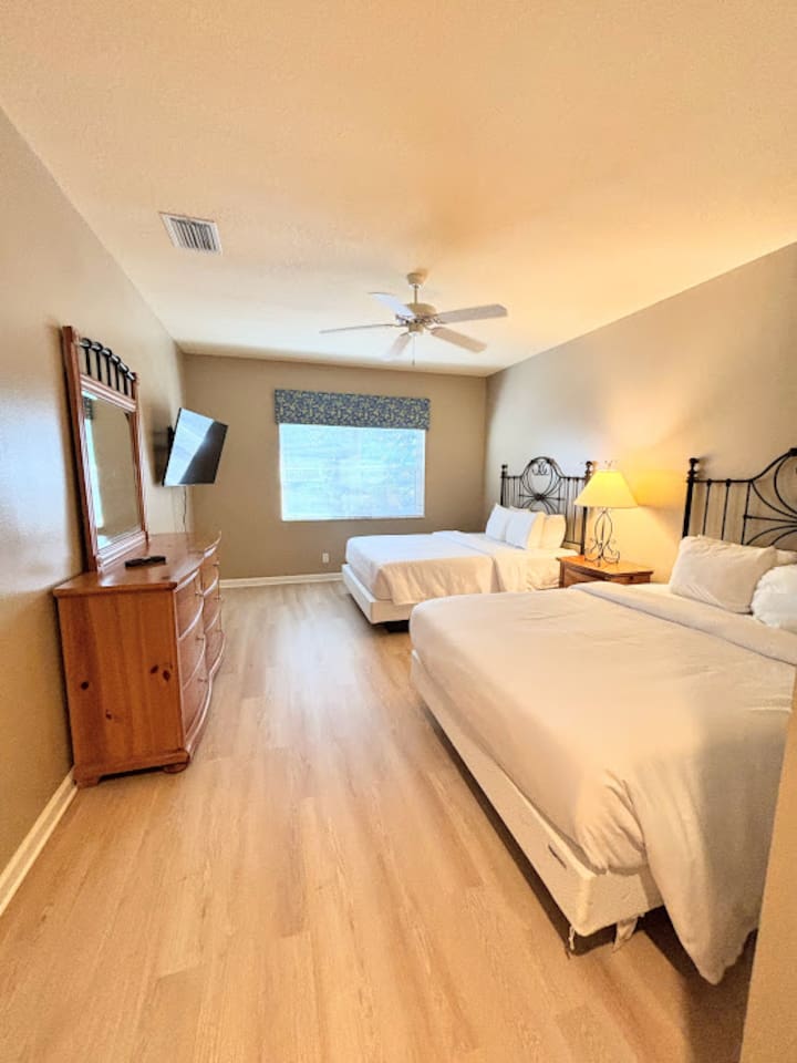 Comfortable bedroom with two beds, wood-look flooring, dresser storage, and a wall-mounted TV.