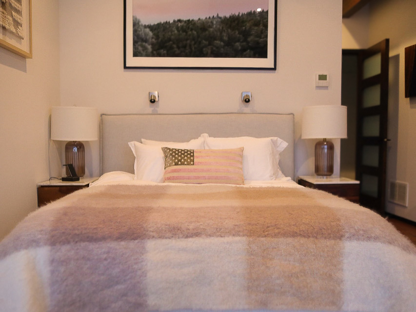 Bedroom Two at Sunset Falls &mdash; upholstered headboard, tripod lamps, framed forest photograph