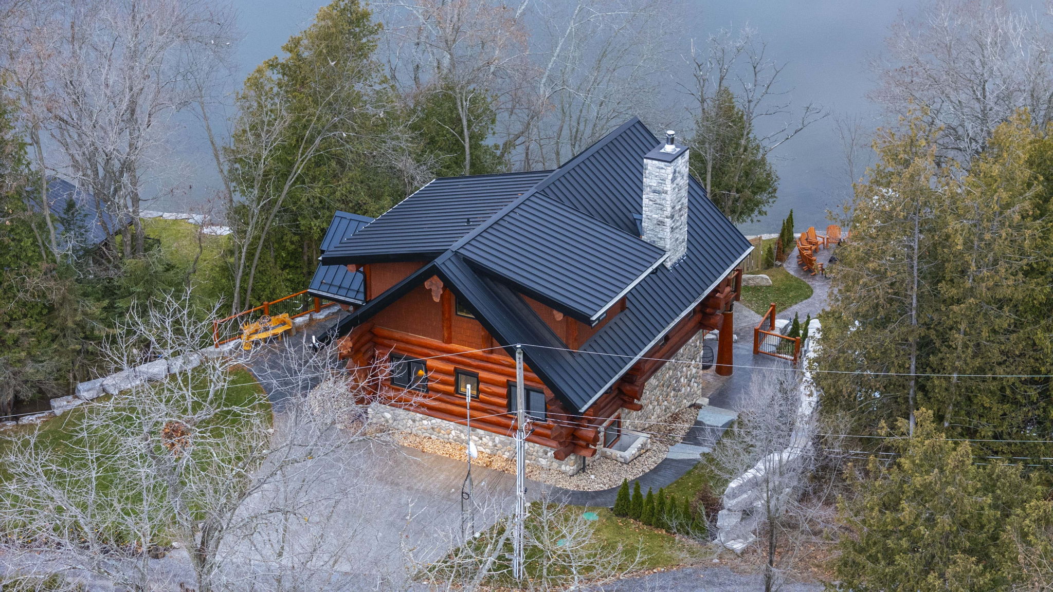 Aerial view of Bear Lodge showing lake access, wrap-around decking, firepit, and private wooded setting.