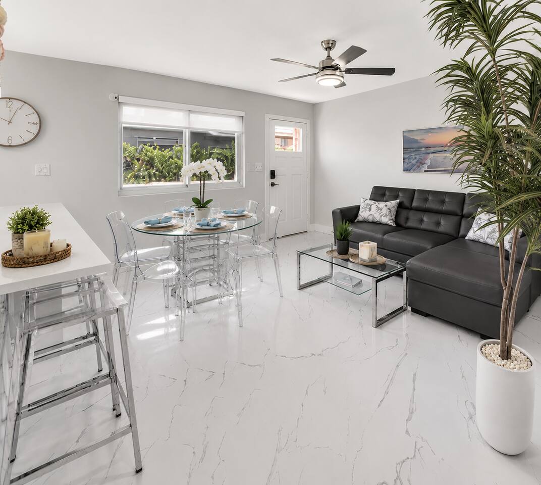 Open-concept living and dining area with a comfortable sectional, dining table for four, breakfast bar seating, and a clean, modern design.