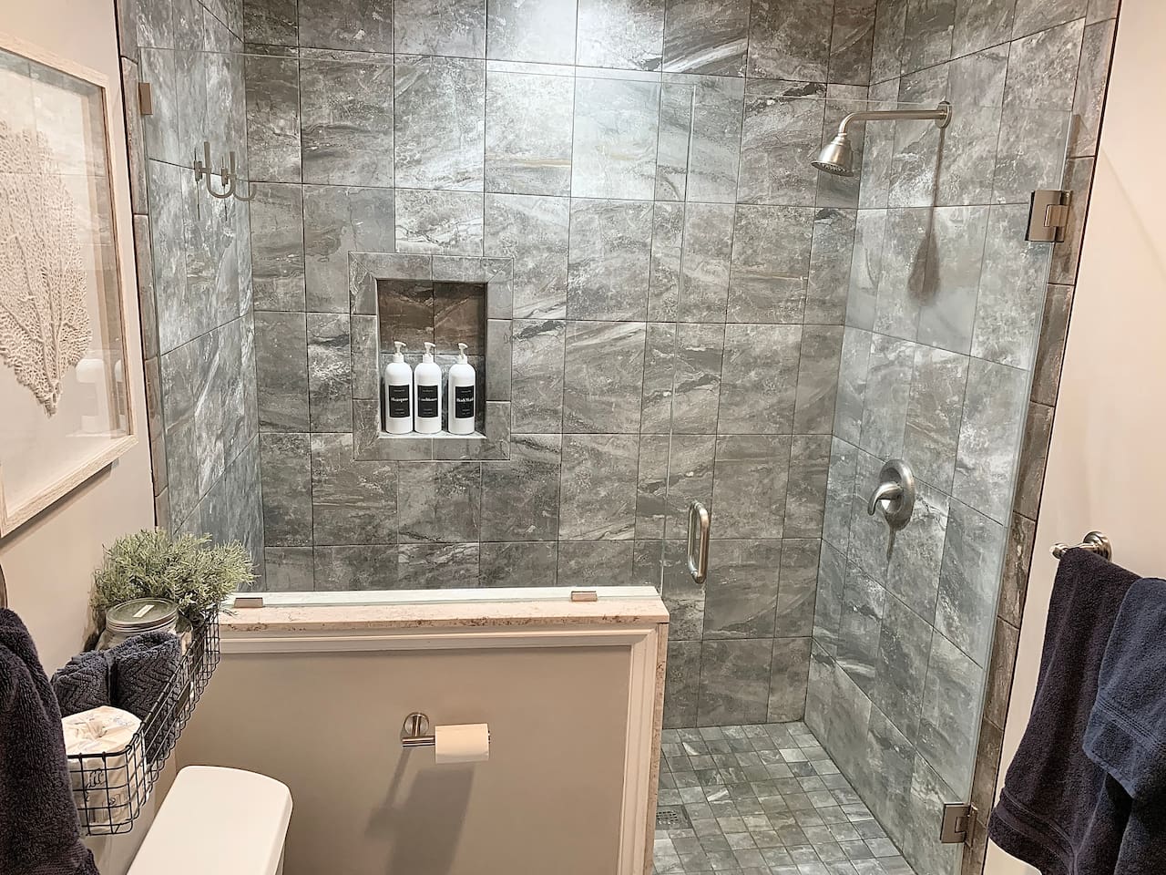 Step into this luxurious glass-enclosed shower, featuring floor-to-ceiling grey marble-style tile and a built-in niche for amenities. The modern fixtures and clean design provide a refreshing, spa-like experience after a day in the sand.