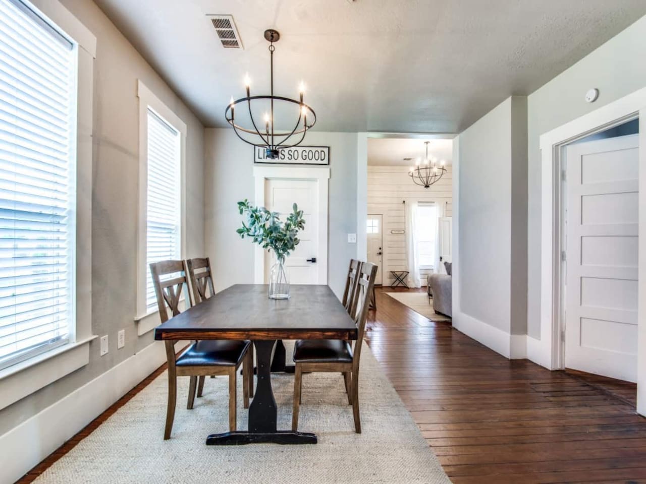 Farmhouse dining table with upholstered chairs, statement chandelier, shiplap accent wall, and hardwood floors. Bright natural light from large windows. Modern farmhouse Airbnb in downtown Aubrey TX steps from S Main Street dining.