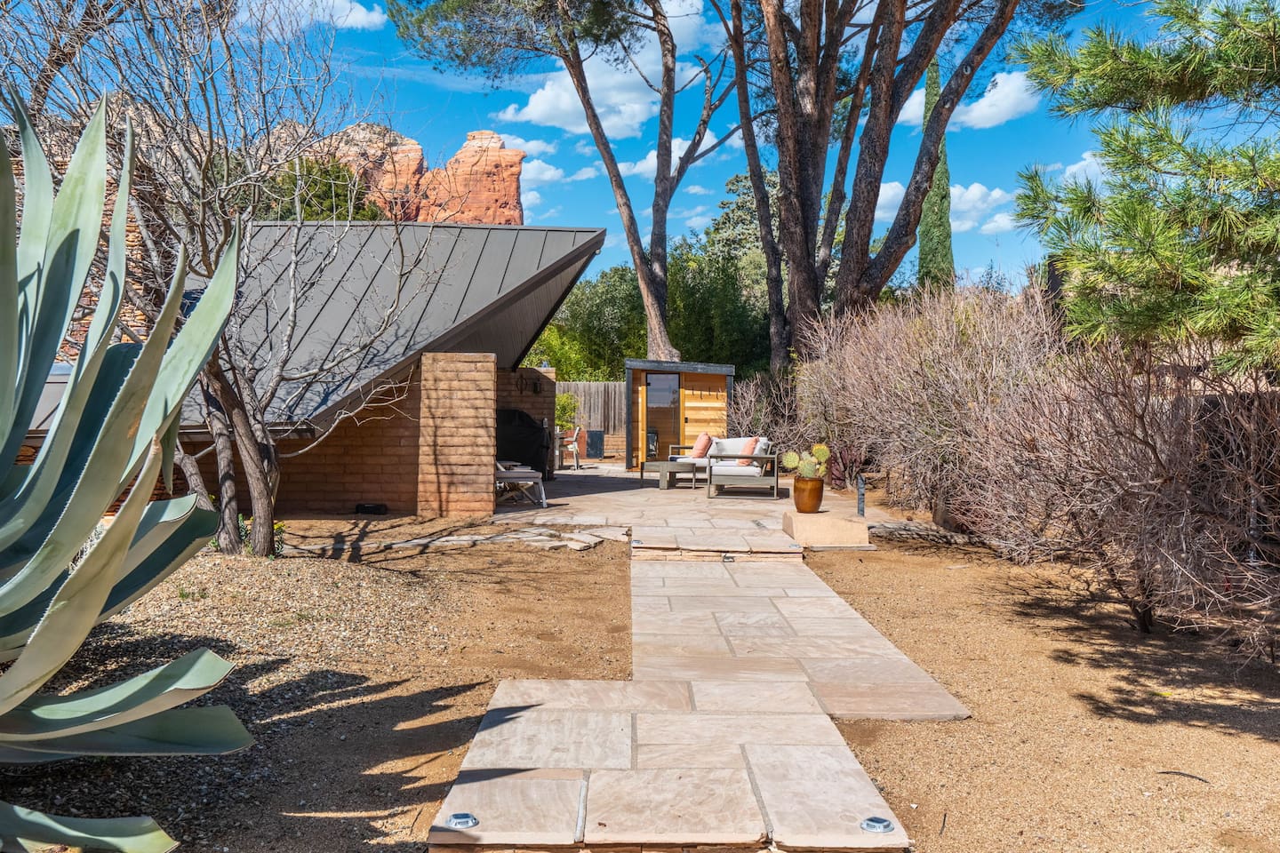Desert-inspired exterior with a stone walkway leading to a private patio, surrounded by native landscaping and red rock views.