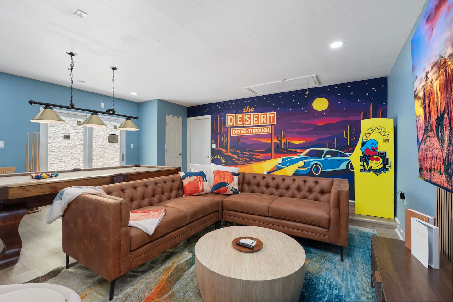 Playroom with vintage desert mural, leather seating, pool table, and arcade games—a fun, colorful space for all ages.