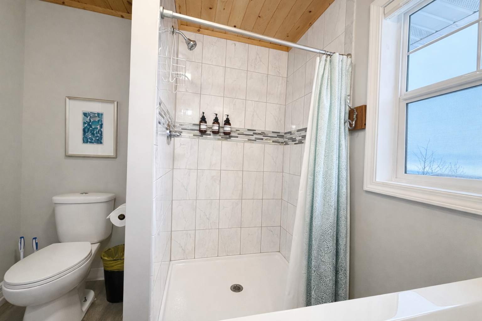 This upstairs bathroom features a crisp, walk-in shower with freshly updated tile. A window opens up to a serene view of Lake Superior, bringing in natural light.