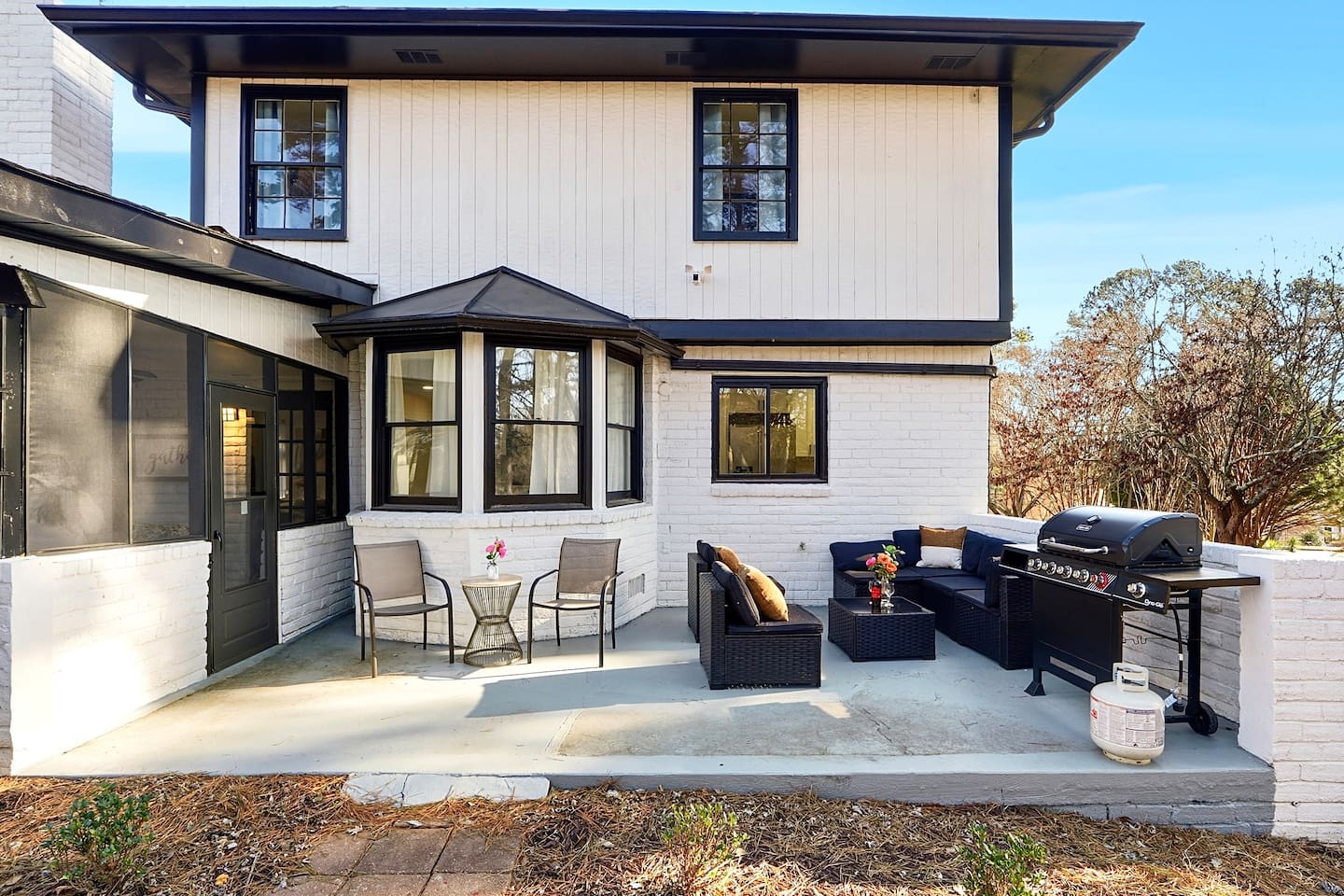 Inviting patio with black outdoor furniture, beige chairs, and a propane grill. A great space to relax, dine outside, or enjoy time with friends and family.