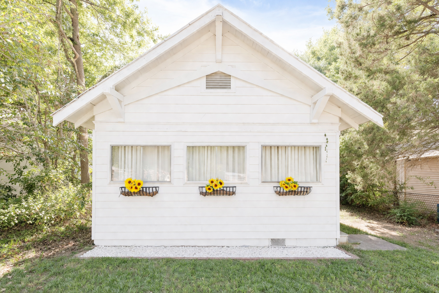 Classic cottage charm framed by lush greenery and sunny blooms, ready to welcome you in.