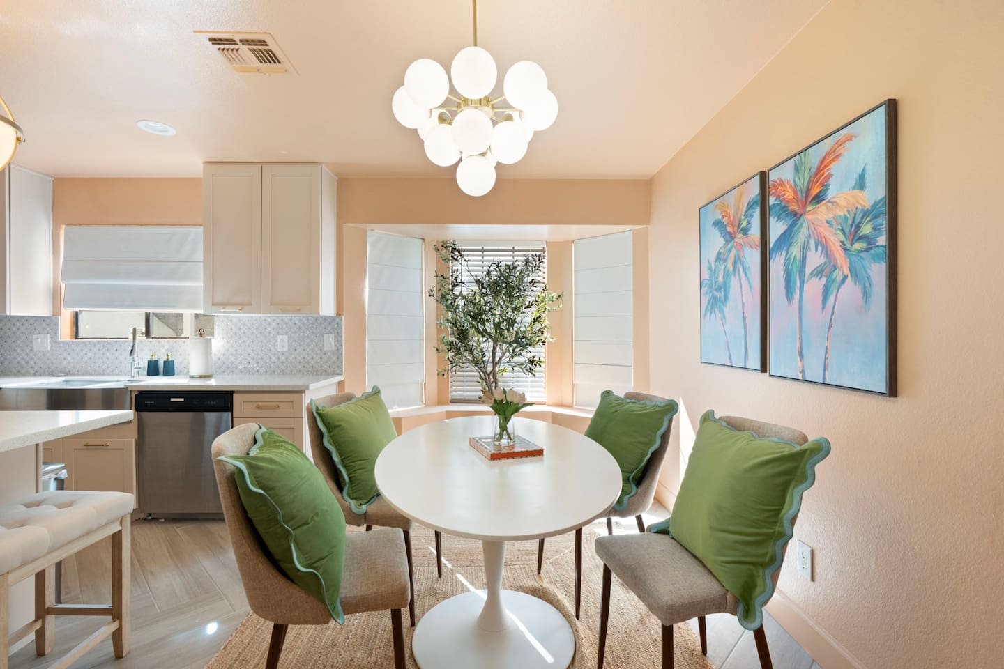 Bright dining nook with round white table, green upholstered chairs, and tropical art—a cheerful space for meals and conversation.