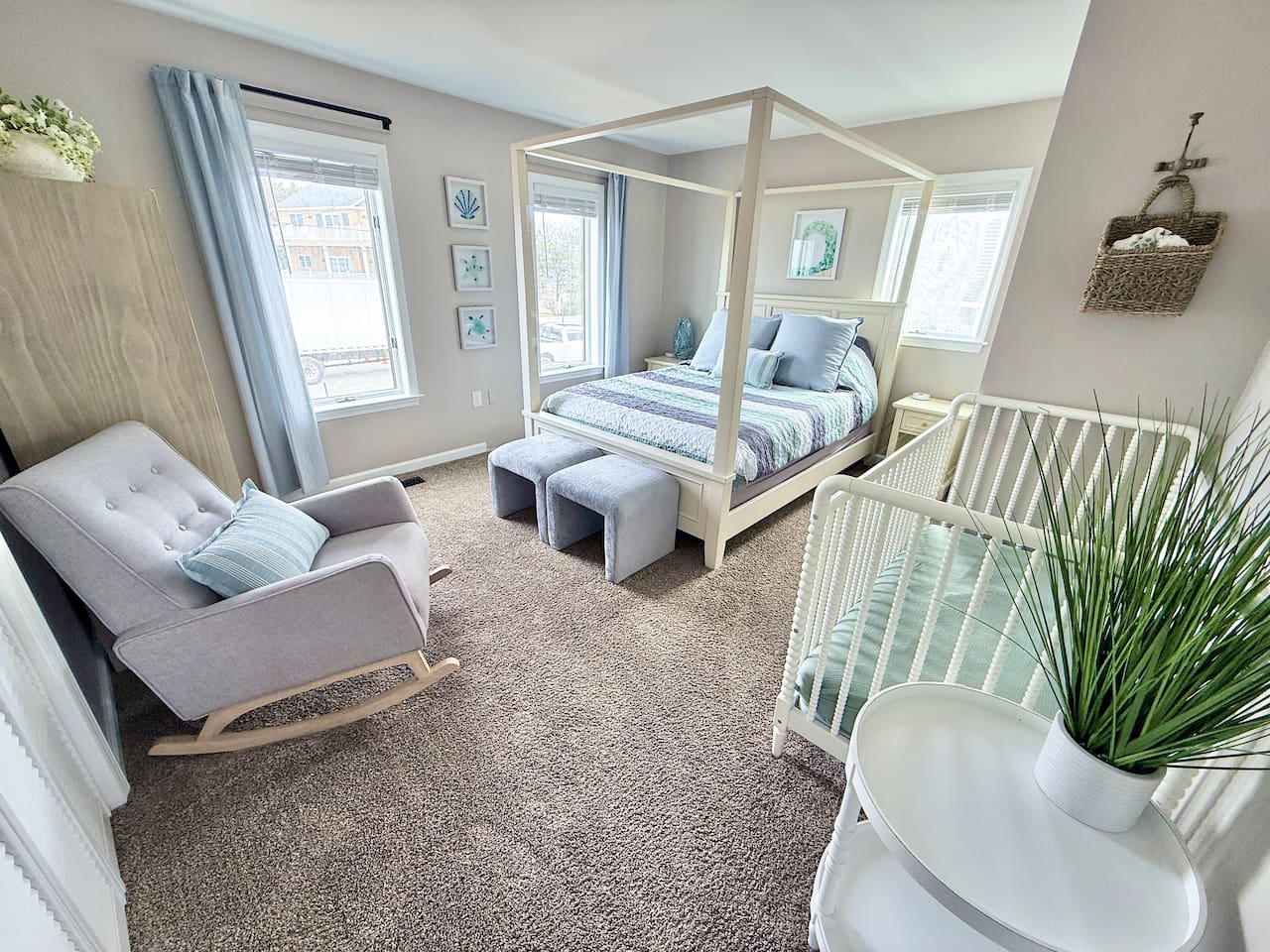 This family-friendly bedroom offers a relaxing, coastal retreat featuring a four-poster canopy bed, a white crib, and a cozy rocking chair. Light blue curtains and nautical art complete the space.