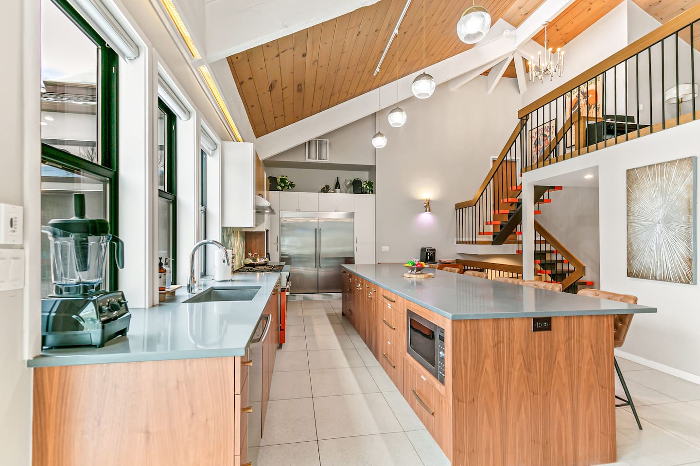 The kitchen is fully equipped with modern appliances, a Mid-Century Modern interior design, a large fridge, freezer, and ample storage. It boasts a spacious layout and a 16 ft island table, with convenient access to the outdoor area.
