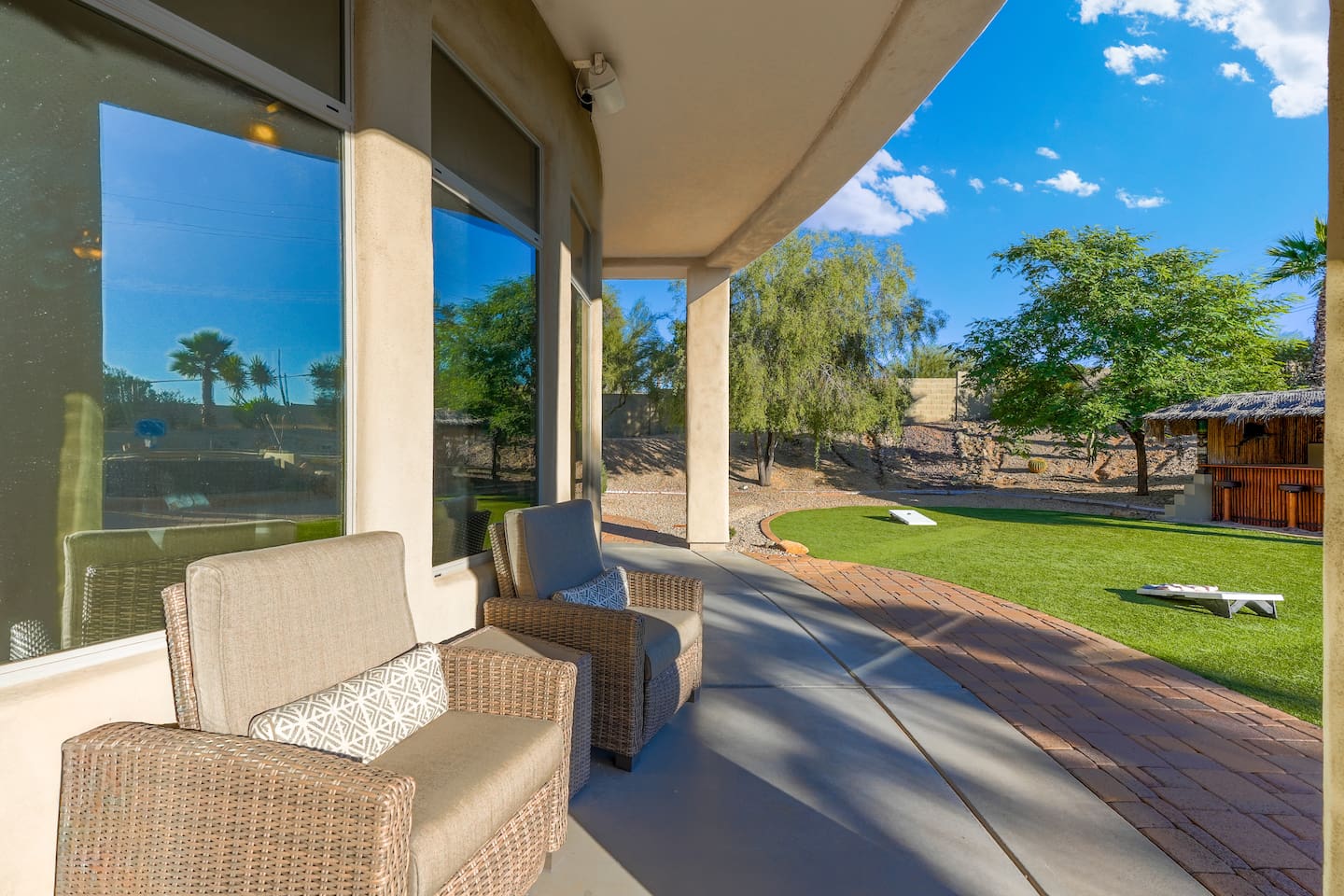 Covered patio perspective overlooking the turf and tiki bar, blending shaded comfort with open backyard views.