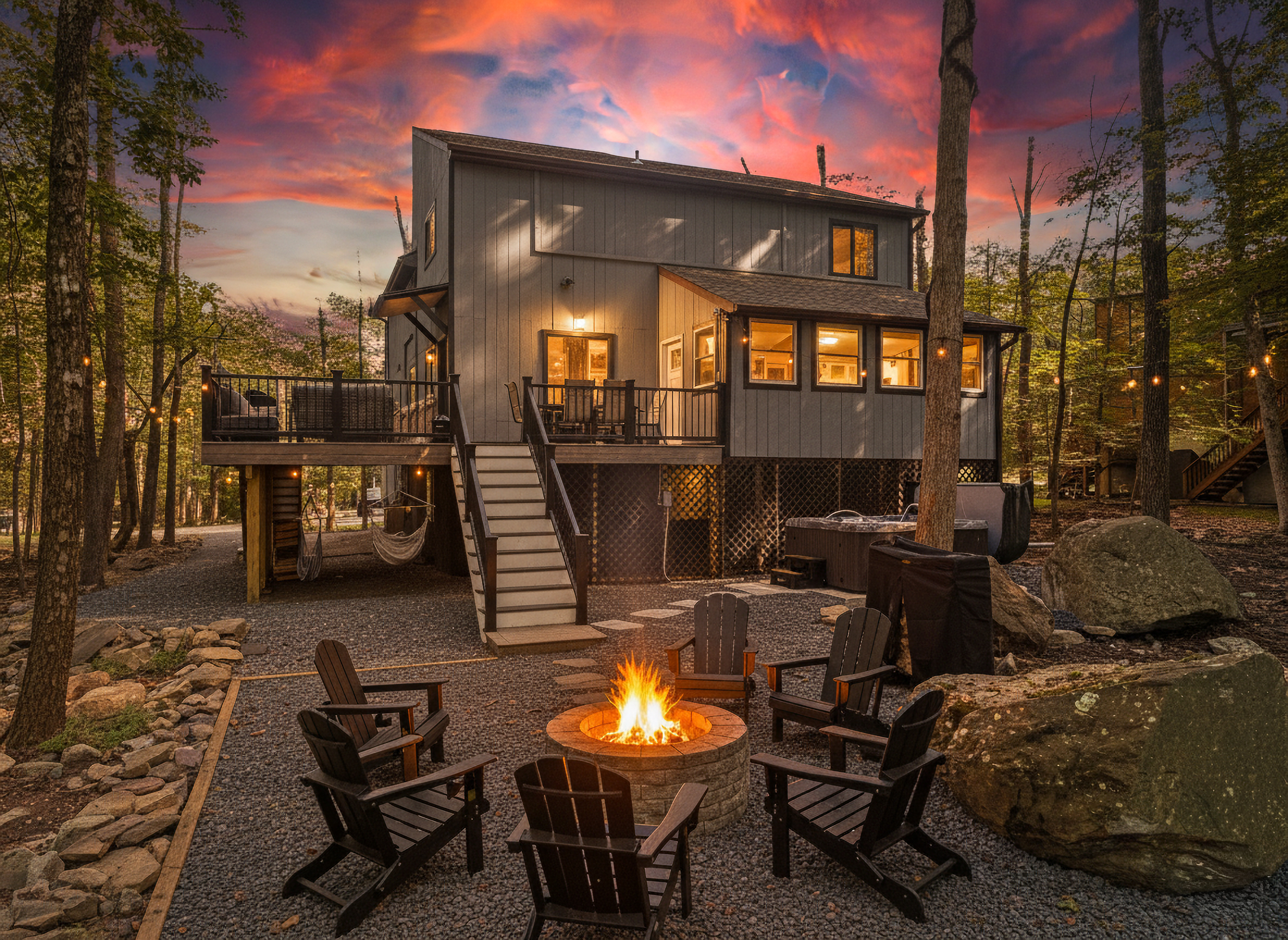  A private outdoor deck with dining space and a stone fire pit set against a wooded backdrop