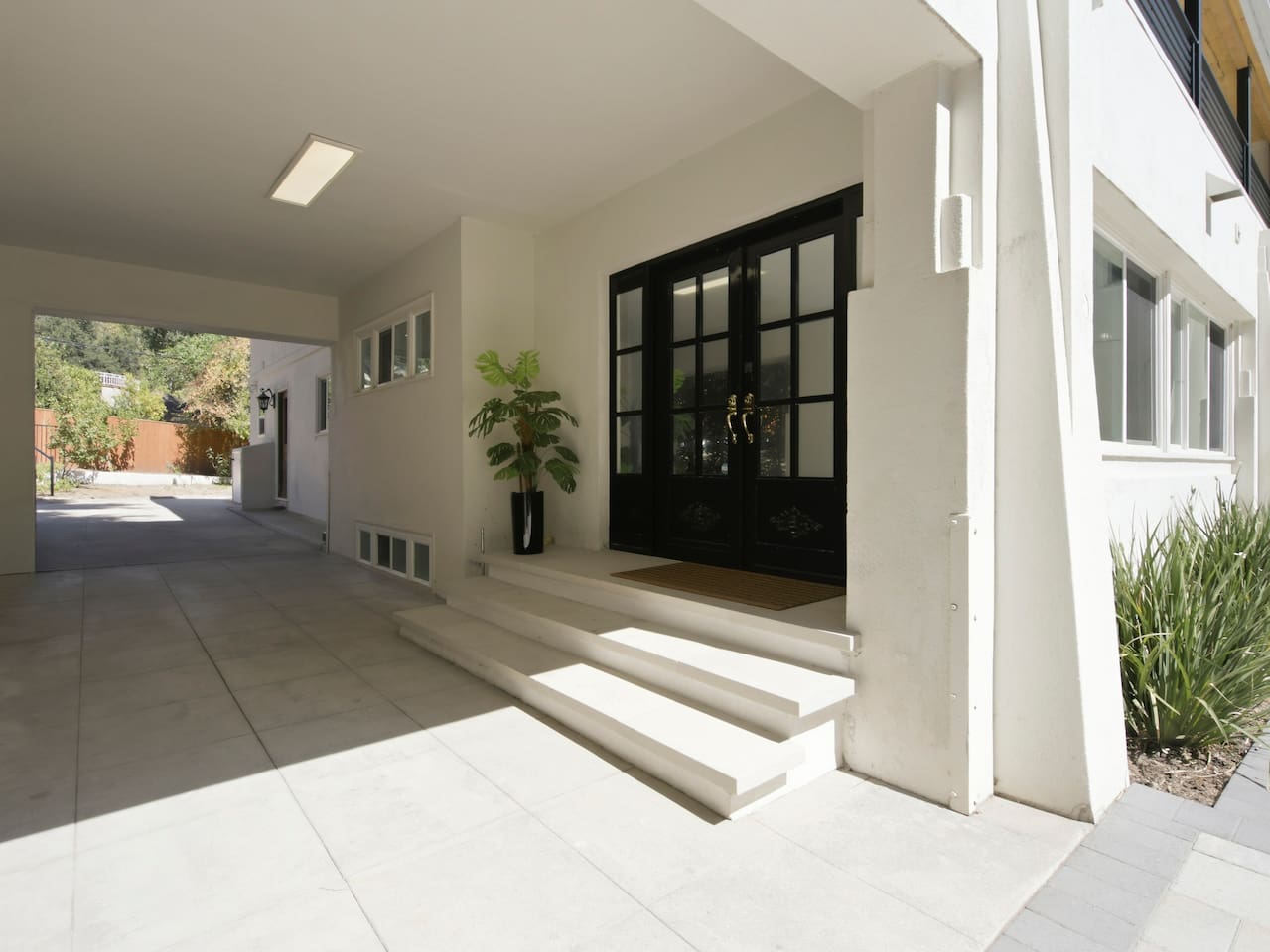 View of the entrance and covered passage framed by greenery visible beyond the property.
